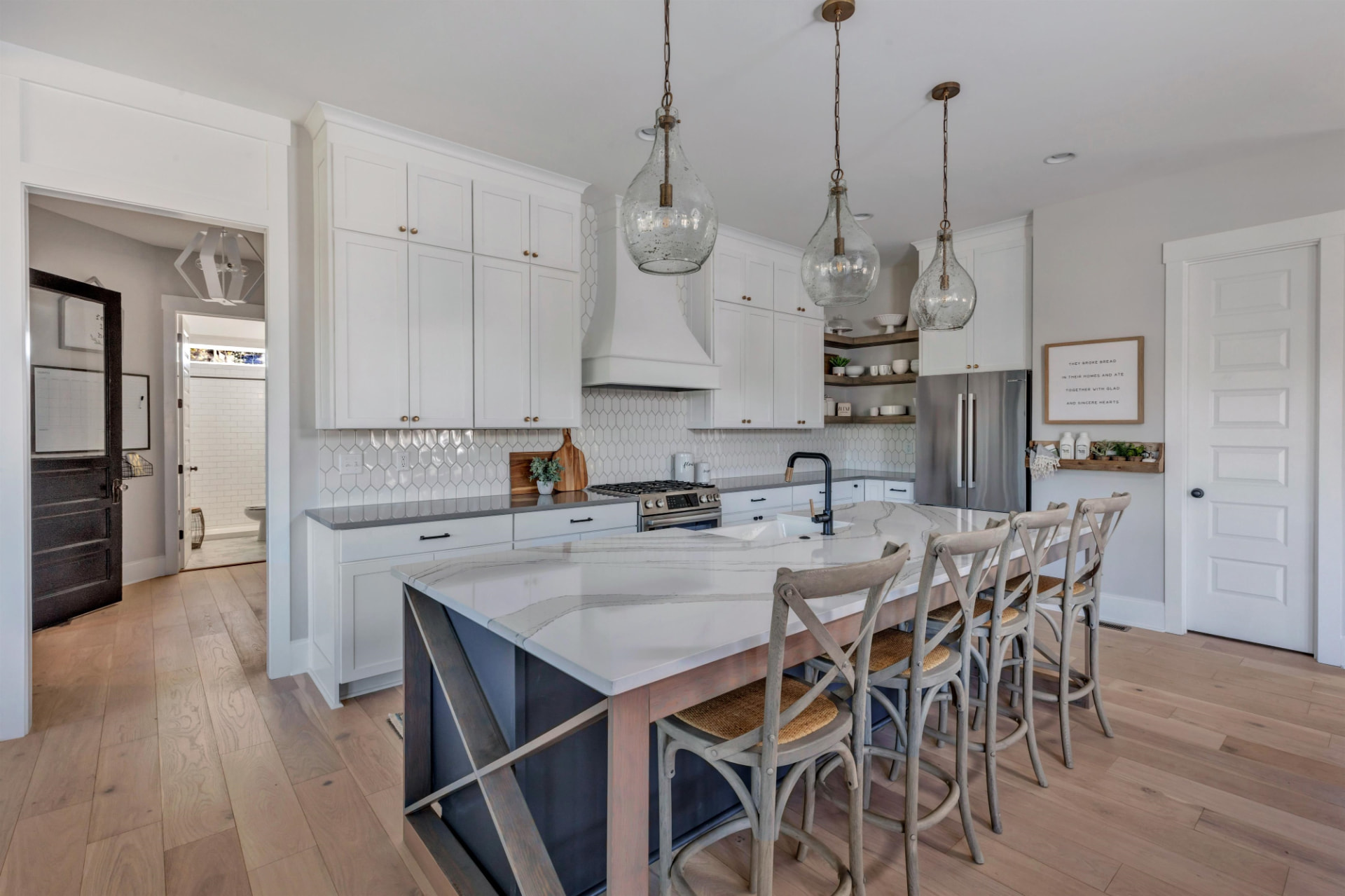 White shaker kitchen with brass hardware, quartz island and glass pendants